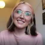 Ellie Middleton - female in a pink top smiling to the camera wearing large glasses and blonde hair with pink at the front
