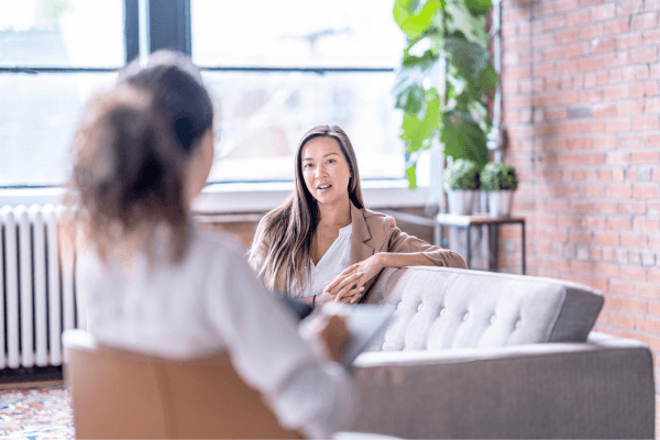 Two ladies talking, one on a sofa and the other on a chair in a bright open room