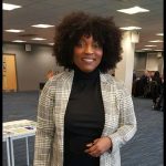 Elizabeth Takyi - a lady with dark hair smiling at the camera. She is wearing a light grey chequed blazer