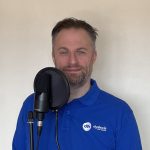 Matt Head in a blue polo standing behind his podcast microphone