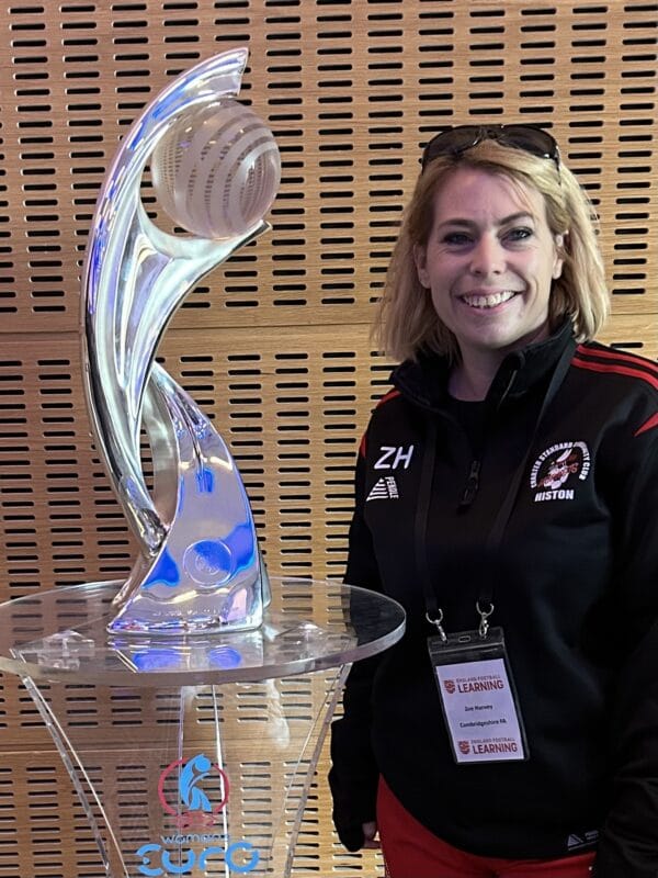 Zoe Harvey, blonde lady in a black football tracksuit standing next to a big football glass trophy