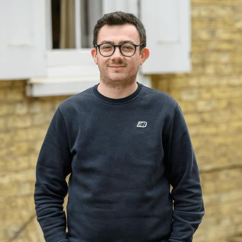 Charlie, man wearing glasses and a dark sweatshirt standing in front of a brick wall