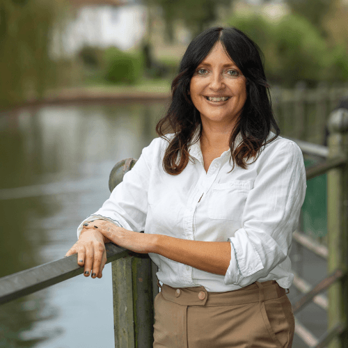 Donna Stevenson - a female with dark brown shoulder length hair wearing a white shirt and camel trousers