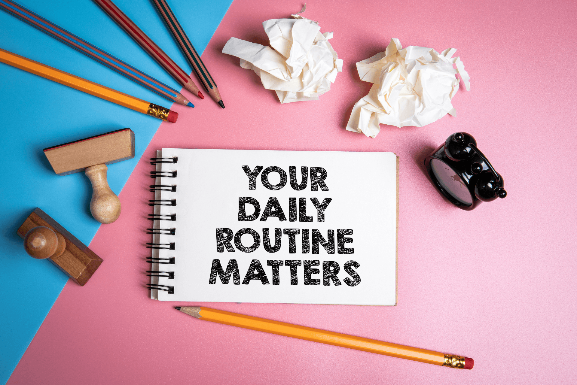 A notepad with 'your daily routine matters' written on the first page, surrounded by pencils and discarded notes