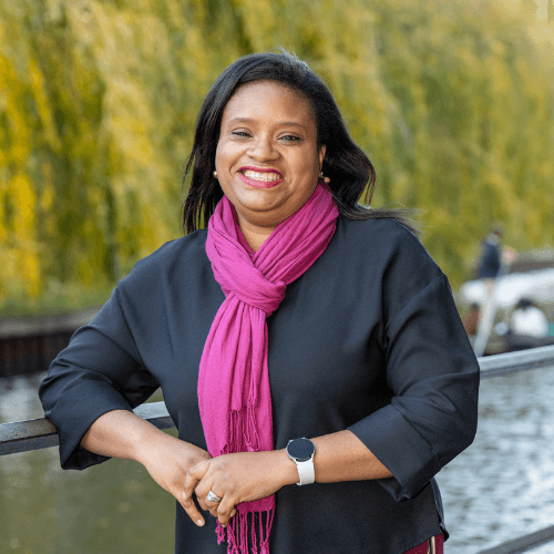 Oly Sanni, A black woman smiling wearing a black top and pink scarf