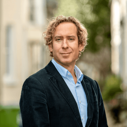 Jason De Turris, A white male wearing a shirt and jacket. He has long curly blonde hair