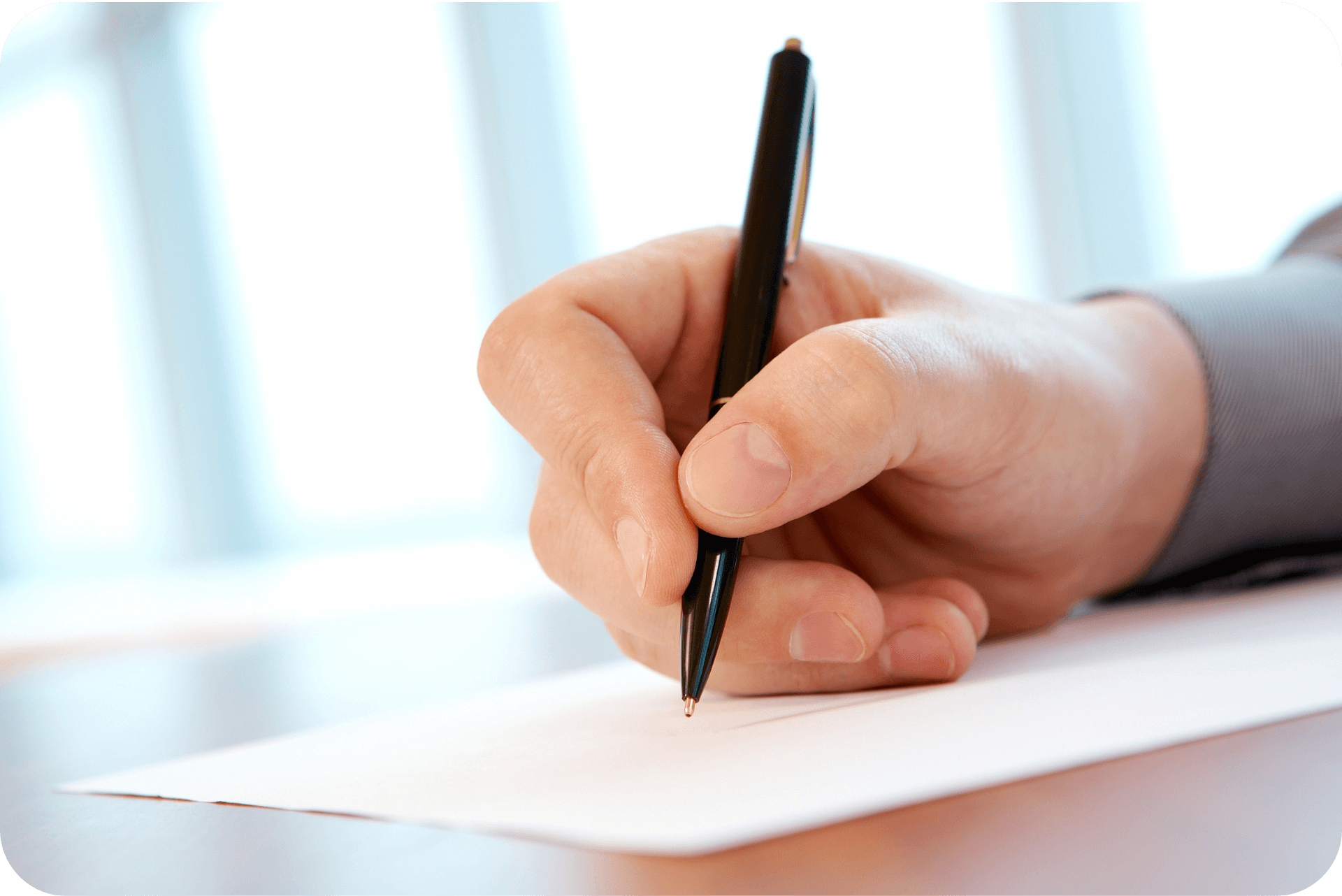 A hand holding a pen, writing on a white piece of paper