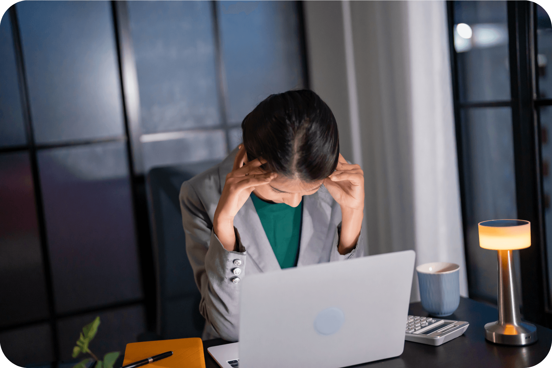 Female office worker wearing a grey blazer and emerald green shirt. The office lighting in has been dimmed.