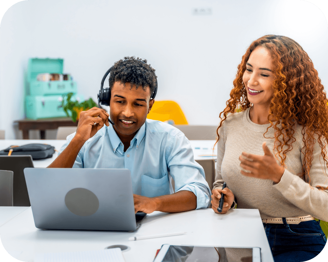 A male and female office worker sitting next to eachother in a office setting, working together on a laptop