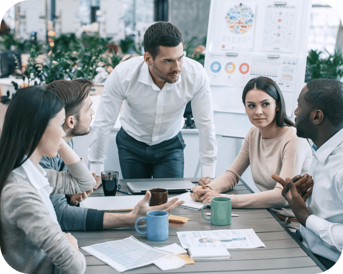 A mixed group of office workers, they are sitting around a desk discussing work