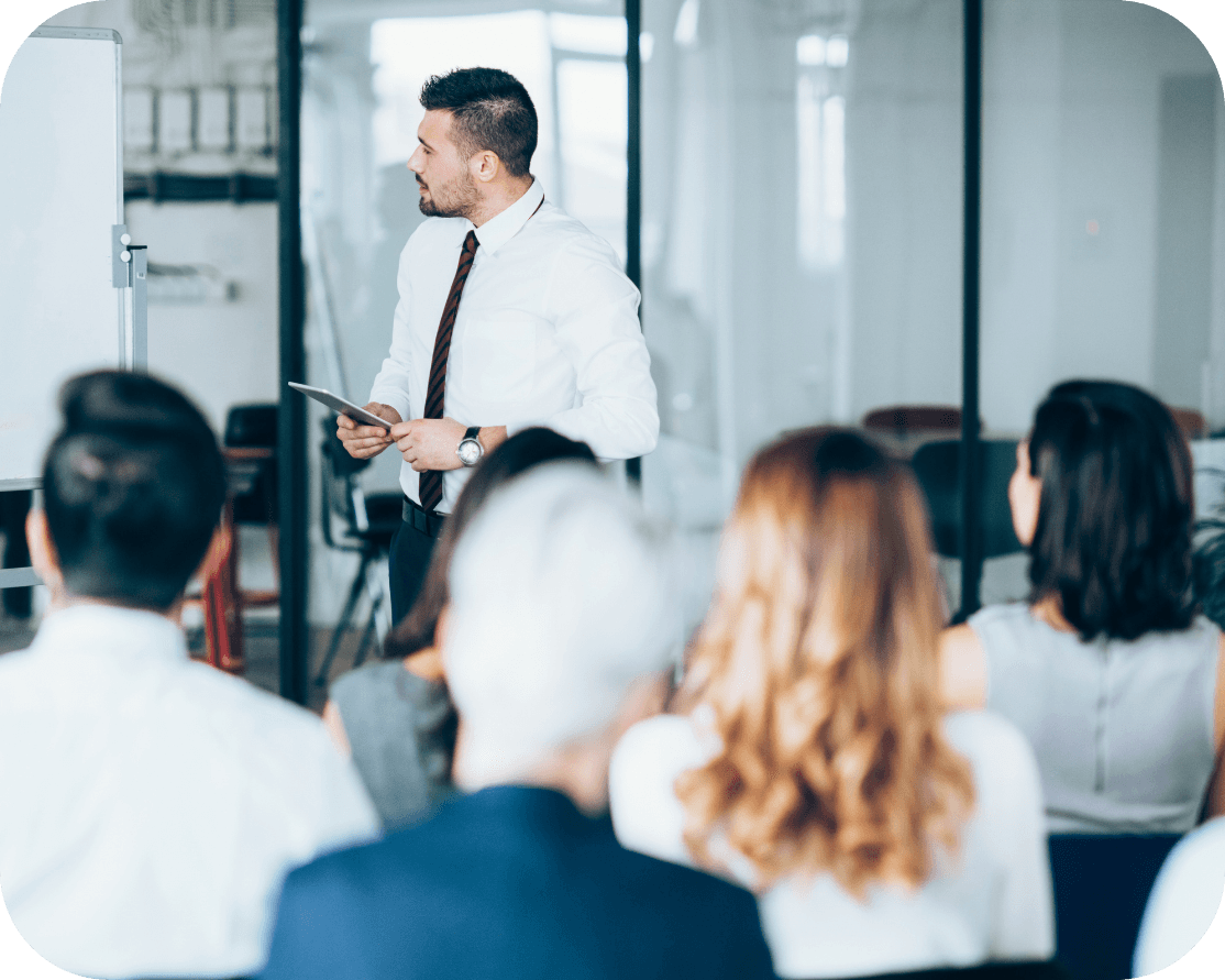 A group of office workers, sitting in a meeting room and watching a presentation