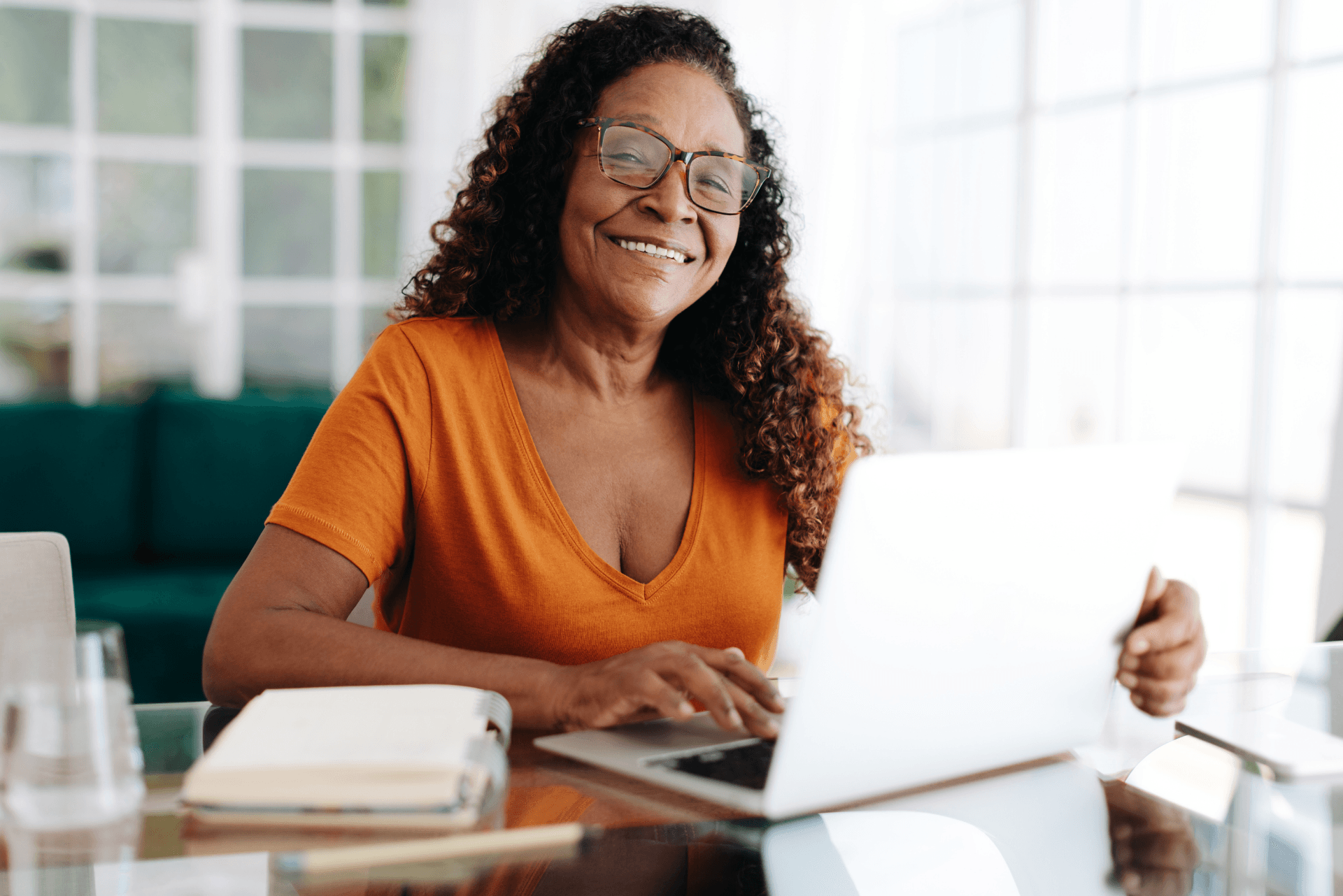 A black woman, smiling while working from home on her laptop