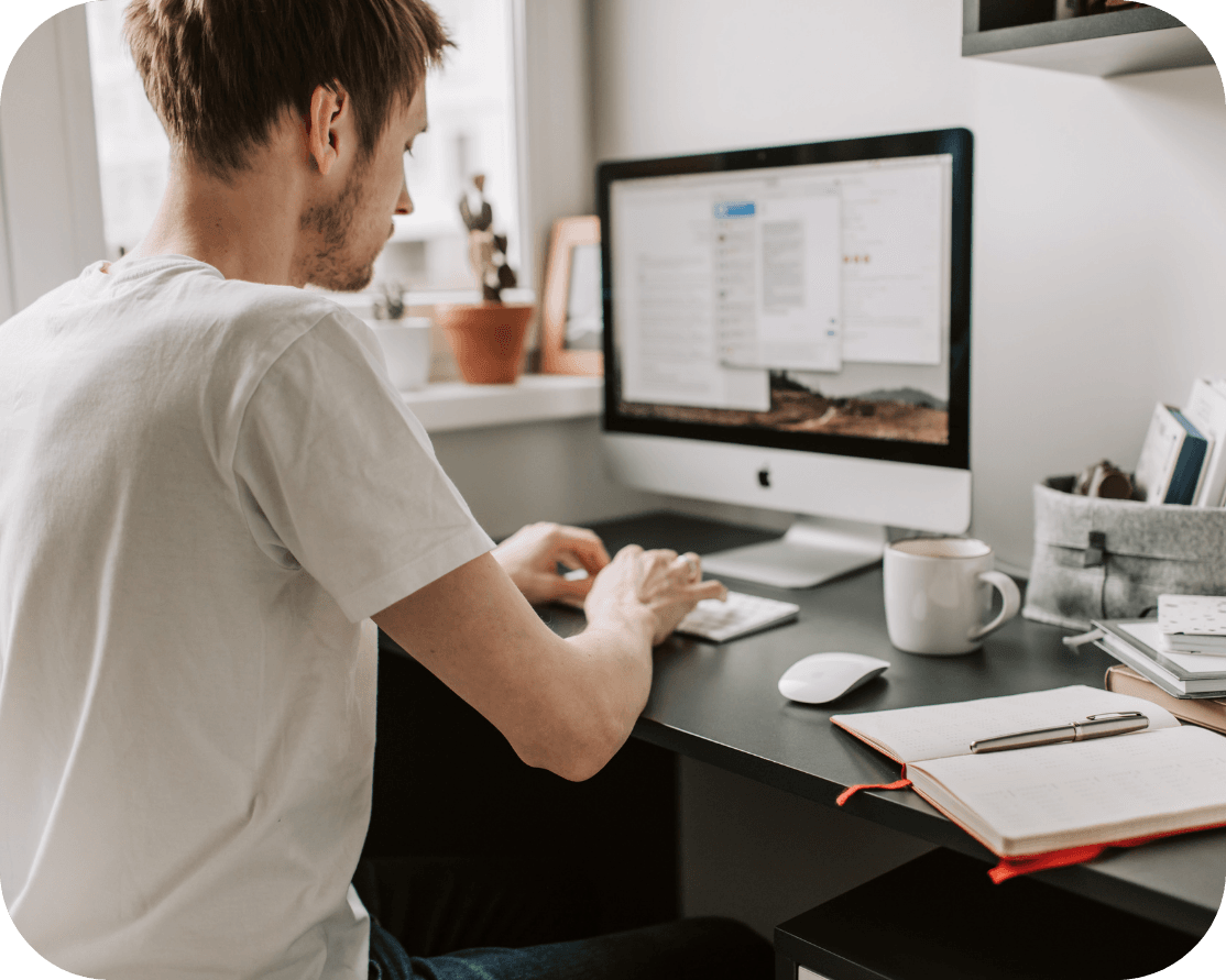 a male wearing a white t-shirt, they are typing on their keyboard in their office space