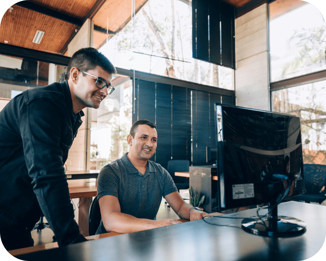 Two males in an office space, wearing grey t-shirts and looking at a computer screen