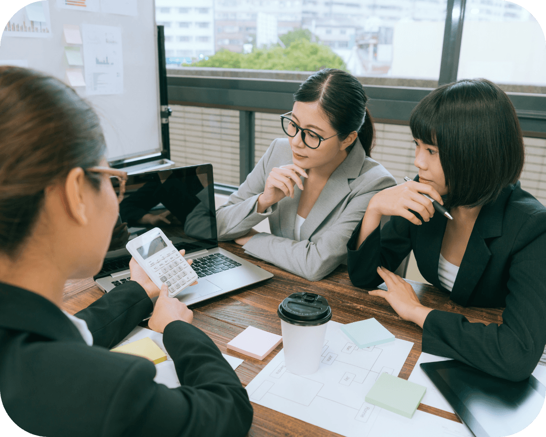 Three woman in black and grey office suits, discussing working displayed on a laptop