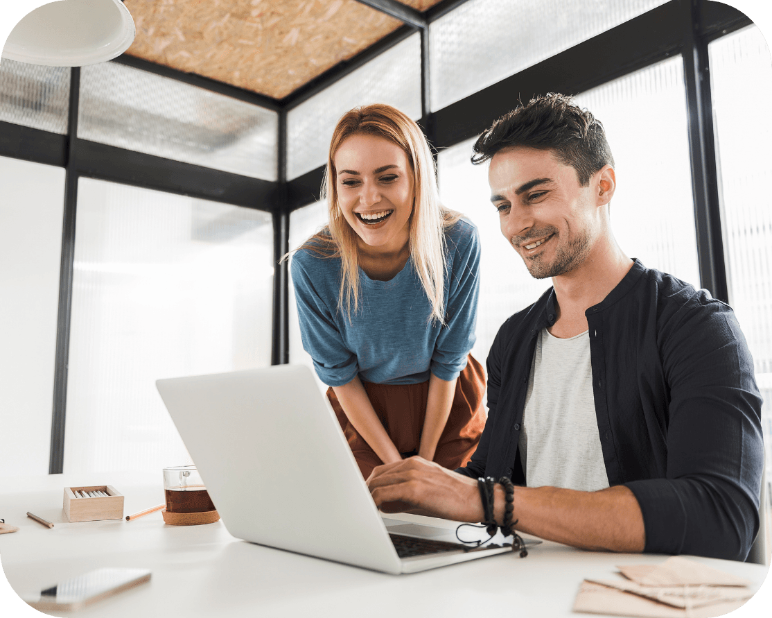 A blonde female smiling next to a male working on a laptop