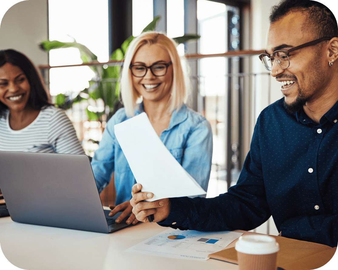 three people sitting together and smiling while working together on a laptop